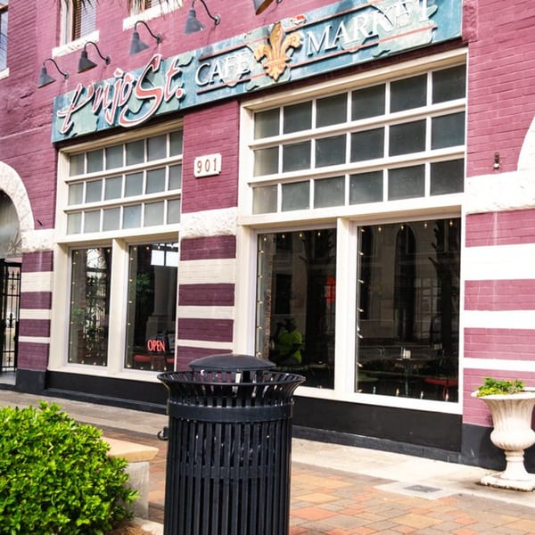 Exterior of Pujo St Cafe, a brick building with large windows and a blue sign.