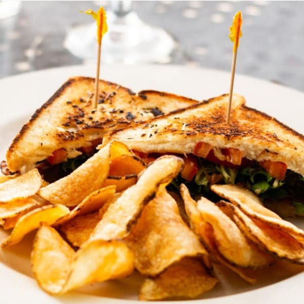Grilled sandwich with lettuce and tomato, served with a side of golden potato chips.