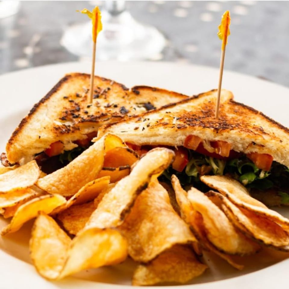 Grilled sandwich with lettuce and tomato, served with a side of golden potato chips.