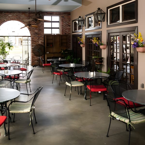The Pujo St Cafe dining room with tables, chairs, brick walls, and large windows.