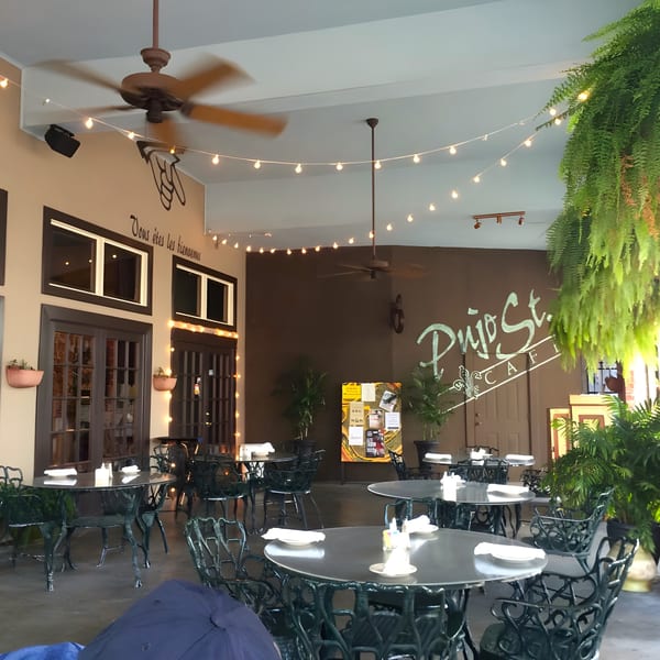 Pujo St Cafe's outdoor patio with black wrought iron tables and chairs, string lights, and lush greenery.