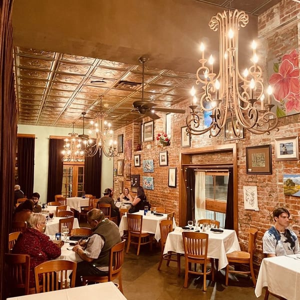 Pujo St Cafe's dining room with brick walls, chandeliers, and patrons enjoying their meals.