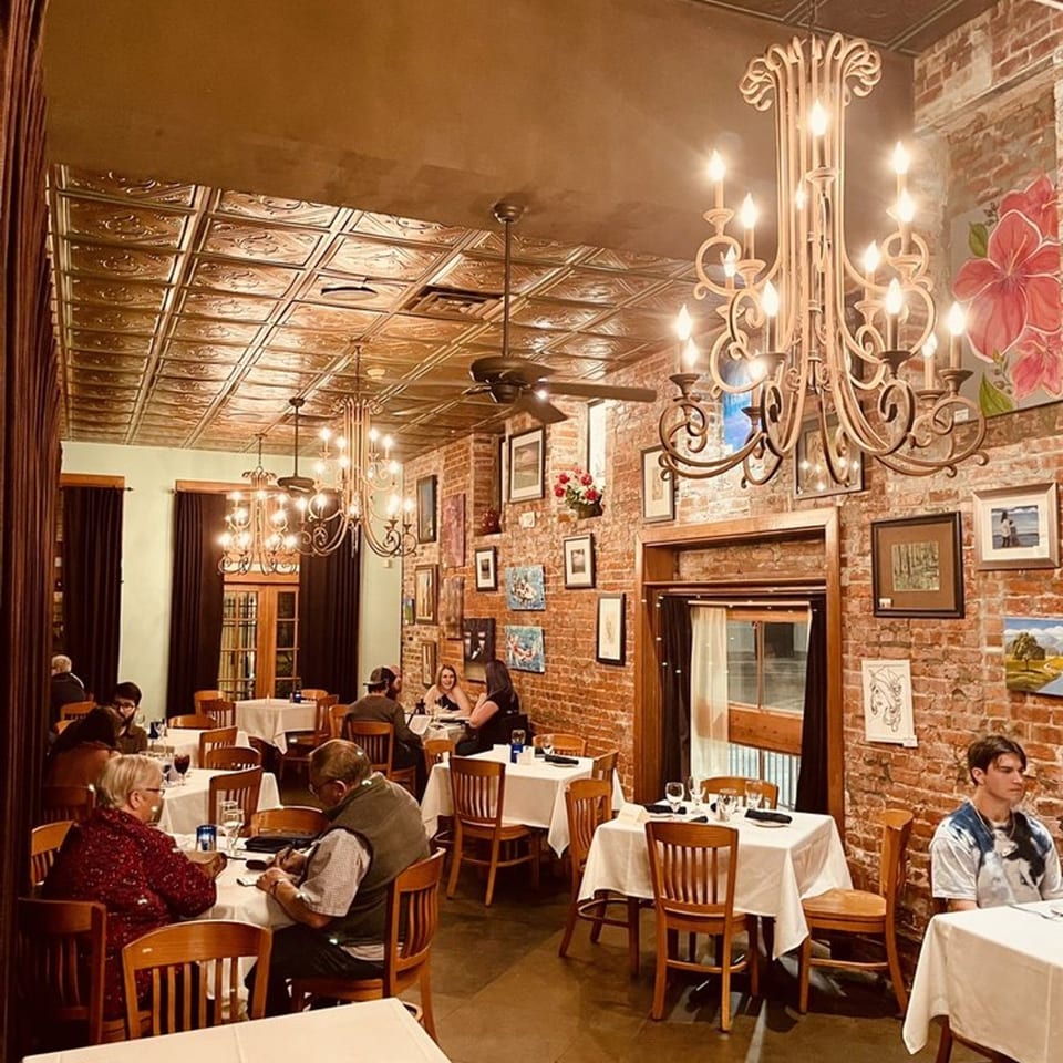 Pujo St Cafe's dining room with brick walls, chandeliers, and patrons enjoying their meals.