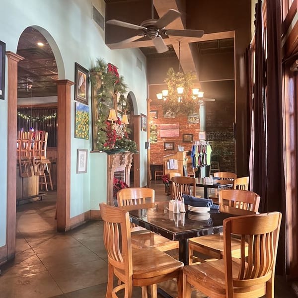 Interior of Pujo St Cafe with wooden tables and chairs, a decorated fireplace, and arched doorways.