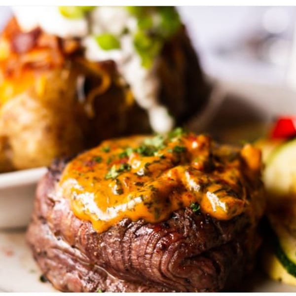 Grilled steak with a creamy orange sauce, served with a loaded baked potato and vegetables.