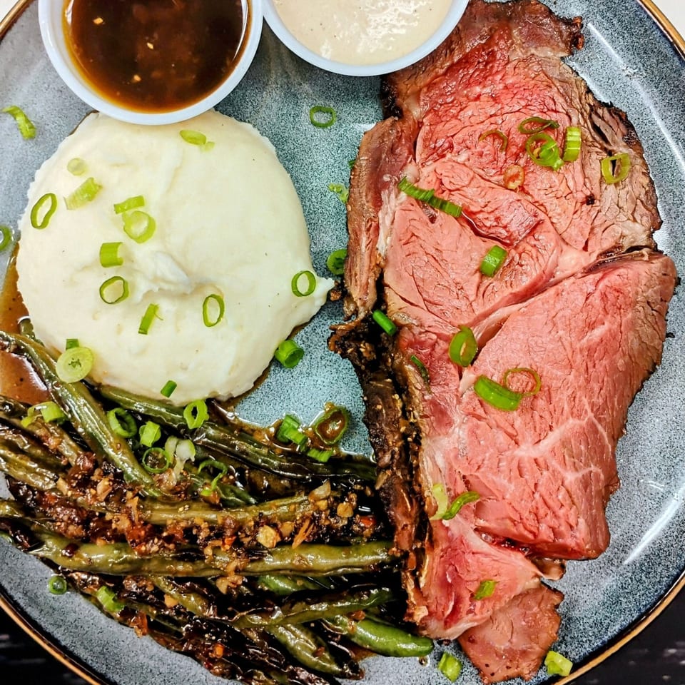 Pujo St Cafe's prime rib with mashed potatoes, green beans, and two dipping sauces.